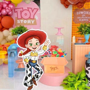 以下が含まれることがあります： ジェシーのカウガールが手を振っている漫画のイメージが特徴の、カラフルなトイ・ストーリーをテーマにしたパーティーデコレーション。画像にはおもちゃの箱と「Toys」と「Toy Story」の文字が含まれています。背景には風船やその他のパーティーデコレーションが含まれています。