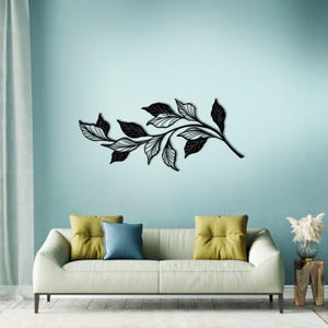 May include: Black metal wall art featuring a stylized branch with leaves. The art is displayed on a light blue wall above a white couch with yellow and blue throw pillows.