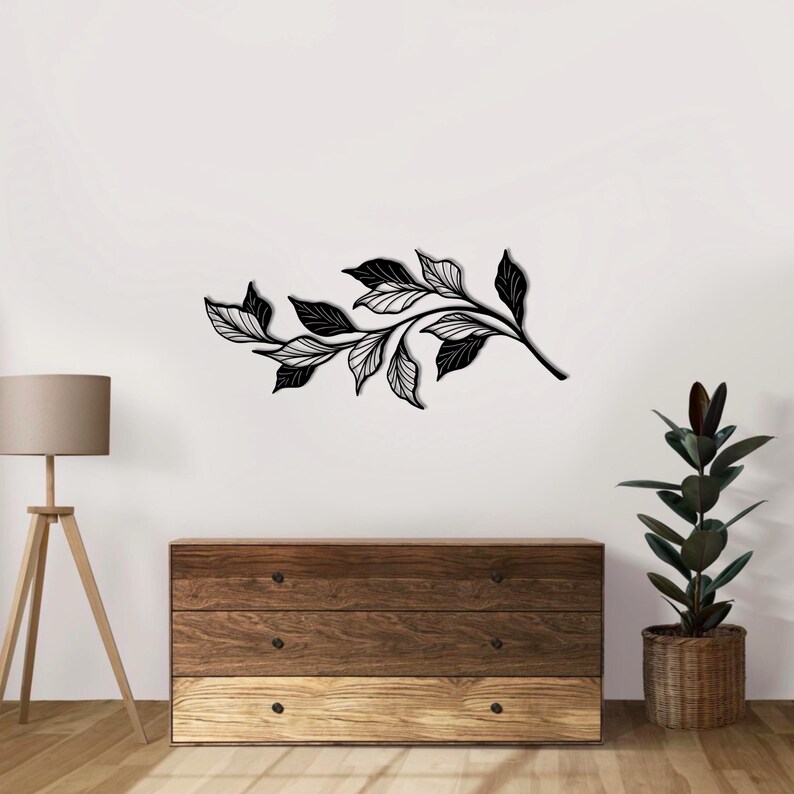 May include: Black metal wall art featuring a stylized branch with leaves. The branch is curved and has a delicate, intricate design. The leaves are arranged in a flowing pattern.
