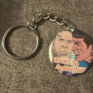 May include: A round keychain featuring a comic book style image of two men with the text "Wow! So beautiful" printed on the bottom.