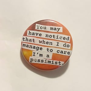 May include: A circular badge with an orange and yellow gradient background. The text on the badge reads, "You may have noticed that when I do manage to care I'm a pessimist."