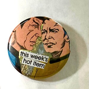 May include: Round button featuring a vintage comic book style image of two men. The button has the text "this week's hot item" in a white font on a white background. The button has a glossy finish and a yellow and green background.