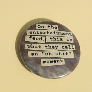 May include: A circular badge with a purple and grey tie-dye pattern. The text on the badge reads: "On the entertainment feed, this is what they call an 'oh shit' moment".