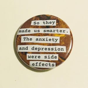May include: A circular badge with a brown and yellow marbled pattern. The text "So they made us smarter. The anxiety and depression were side effects" is printed in white, sans-serif font.
