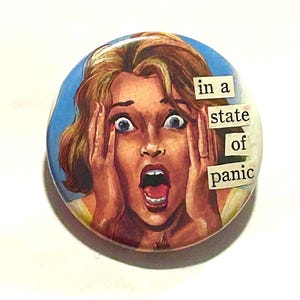 May include: A circular badge featuring a vintage illustration of a woman in a state of panic, with wide eyes and open mouth. Text on the badge reads "in a state of panic". The background is blue.