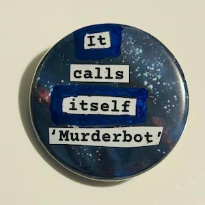 May include: A circular badge with a dark blue and white galaxy pattern. The text "It calls itself 'Murderbot'" is displayed in white block letters, with blue rectangular highlights behind the words.