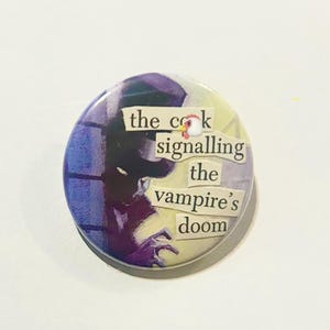May include: A circular badge with a collage design. The badge has a purple and blue background with a figure silhouette. Text on the badge reads "the cock signalling the vampire's doom". A small chicken graphic is included.