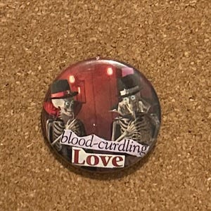 May include: A round button with a red and black background featuring two skeleton figures in top hats. The text "blood-curdling Love" is printed on the button.