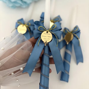 May include: Baptism candles with blue satin ribbons and gold detailing. Each candle features a gold tag with the name "George Antonio", the date "January 12, 2024", and the city "ROME, ITALY". The candles are white and have a spiral design.
