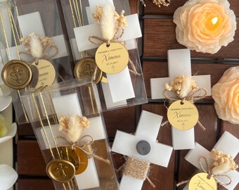 Puede incluir: Velas blancas en forma de cruz con sellos de cera dorada y un pequeño ramo de flores secas. Las velas están empaquetadas en cajas transparentes con cinta dorada. Las cajas también incluyen un círculo dorado con el texto "PRIMERA COMUNION Ximena 01.24.2021".