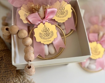 May include: Pink tulle bags filled with white candy and tied with pink ribbon. Each bag has a gold circular tag with Arabic calligraphy and the text "Eid Mubarak".
