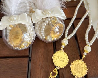 May include: Two white pearl and gold prayer beads with a white feather and bow on top. The beads are in clear glass containers. The prayer beads are attached to a gold charm with the text "Welcome Baby Farah".