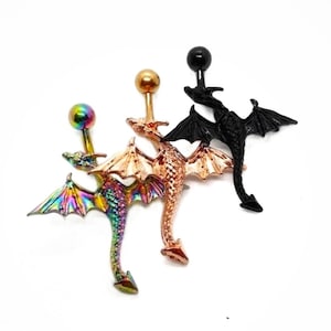 Może przedstawiać: Trzy kolczyki do pępka w kształcie smoka w kolorze iryzującym, różowego złota i czarnym. Każdy smok ma kulisty wierzch i szczegółowe skrzydła. Kolczyki do pępka zaprojektowano w stylu fantasy.