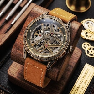 May include: A skeleton watch with a brown leather strap. The watch face showcases intricate mechanical parts in gold and silver hues. The watch is presented on a wooden stand. The text "ARTISAN MECHANICS EST. 1898" is visible.