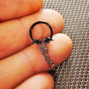 May include: Black metal septum ring with a dangling bat and red gem accents.