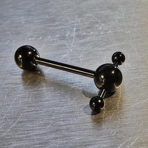 May include: A black barbell body piercing. It features a central sphere with three smaller spheres attached, and a larger sphere on the opposite end of a straight bar. The jewellery is made of a shiny, dark material.