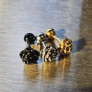 May include: Three rose-shaped earrings with a stud post. The earrings are gold, silver, and black.