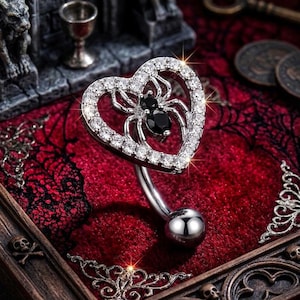 May include: A silver belly button ring featuring a heart-shaped design with a spider inside. The heart is encrusted with clear crystals, and the spider has a black gem body. The ring has a curved barbell and a small silver ball at the bottom.