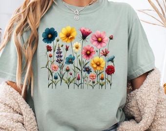 Może przedstawiać: Jasnozielony t-shirt z nadrukiem kwiatowym przedstawiającym różnorodne kolorowe kwiaty, w tym różowe, żółte, niebieskie i czerwone.