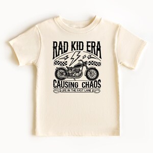 May include: A cream coloured t-shirt with a black graphic of a motorcycle and the text "Rad Kid Era Causing Chaos Life in the Fast Lane".