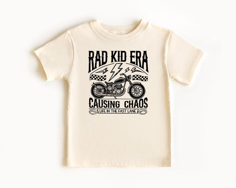 May include: A cream coloured t-shirt with a black graphic of a motorcycle and the text "Rad Kid Era Causing Chaos Life in the Fast Lane".