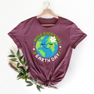 May include: A maroon t-shirt with a graphic of a smiling cartoon Earth with a daisy on top. The text "Make Every Day Earth Day" surrounds the Earth.
