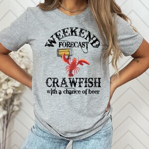 May include: Gray t-shirt with a distressed graphic design that says "Weekend Forecast Crawfish with a chance of beer". The graphic includes a cartoon crawfish holding a beer.