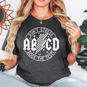 May include: A dark gray t-shirt with a white circle graphic that says "Don't Stress, A-B-C-D, Rock The Test" with a lightning bolt and stars.