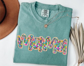 May include: A teal blue t-shirt with a floral design that spells out "Mama".