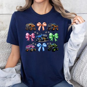 Puede incluir: Camiseta azul marino con un dise&ntilde;o de monster trucks y lazos. El dise&ntilde;o incluye monster trucks naranjas, azules, verdes y rosas con lazos a juego. Un dise&ntilde;o divertido para los fan&aacute;ticos de los monster trucks.