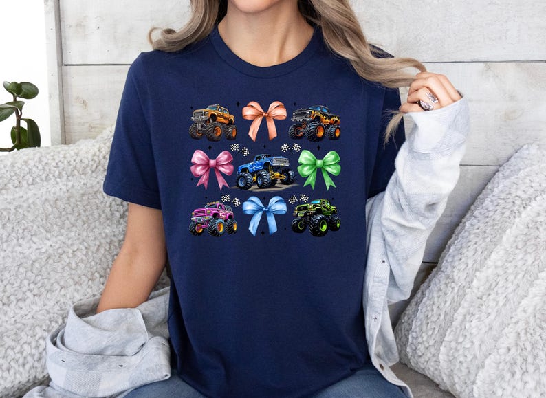 Puede incluir: Camiseta azul marino con un dise&ntilde;o de monster trucks y lazos. El dise&ntilde;o incluye monster trucks naranjas, azules, verdes y rosas con lazos a juego. Un dise&ntilde;o divertido para los fan&aacute;ticos de los monster trucks.