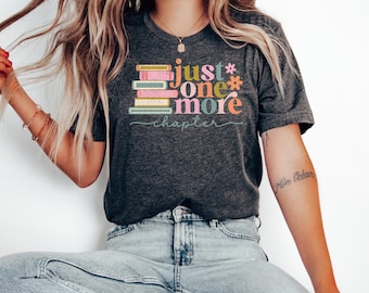 May include: A dark gray t-shirt with a colorful graphic of stacked books and the text "Just one more chapter".
