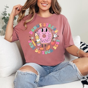 May include: A pink t-shirt with a donut graphic and the text "Donut Stress Just Do You Best". The donut is wearing a graduation cap and holding a pencil.
