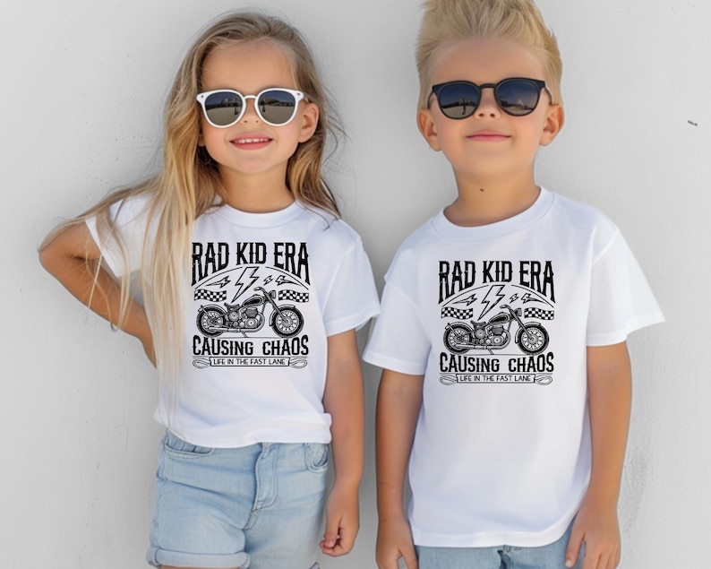 May include: Two children wearing white t-shirts with a black and white graphic of a motorcycle and the text "Rad Kid Era Causing Chaos Life in the Fast Lane".