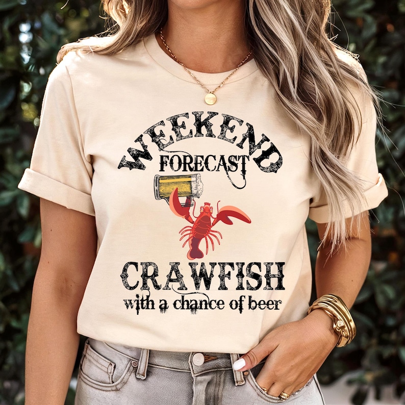 May include: A beige t-shirt with a black graphic that says "Weekend Forecast Crawfish with a chance of beer". The graphic includes a cartoon crawfish holding a beer mug.