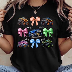 Puede incluir: Camiseta negra con un dise&ntilde;o de monster trucks y lazos coloridos. El gr&aacute;fico incluye lazos naranjas, rosas, azules y verdes, y monster trucks en naranja, azul, rosa y verde. Un dise&ntilde;o divertido y llamativo.