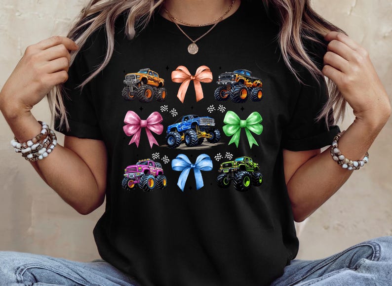 Puede incluir: Camiseta negra con un dise&ntilde;o de monster trucks y lazos coloridos. El gr&aacute;fico incluye lazos naranjas, rosas, azules y verdes, y monster trucks en naranja, azul, rosa y verde. Un dise&ntilde;o divertido y llamativo.