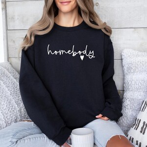 May include: A black sweatshirt with the text "homebody" in white lettering and a small white heart.