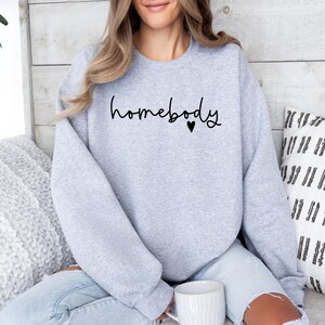 May include: A grey sweatshirt with the text "homebody" and a small heart in black.