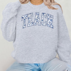 May include: Gray sweatshirt with the word "TEACH" in blue and white floral print.