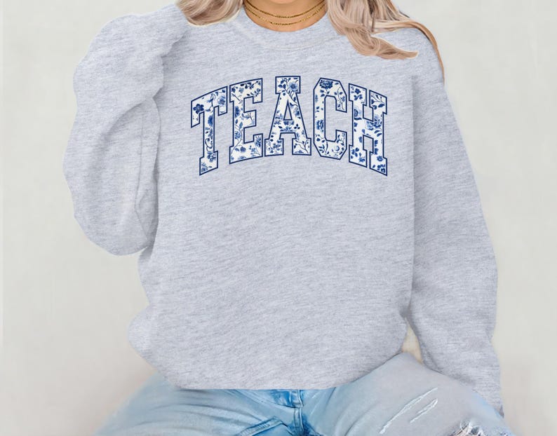 May include: Gray sweatshirt with the word "TEACH" in blue and white floral print.