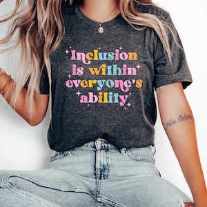 May include: A dark grey t-shirt with the text "Inclusion is within everyone's ability" in colorful letters. The text is surrounded by small white stars.