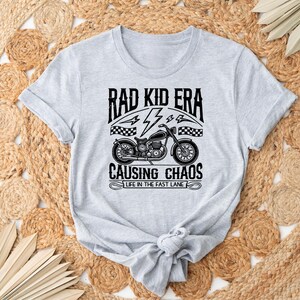 May include: Grey t-shirt with a black and white graphic of a motorcycle and the text "Rad Kid Era Causing Chaos Life in the Fast Lane"