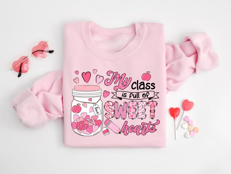 Pu&ograve; includere: Felpa rosa con una grafica di un barattolo pieno di cuori e il testo "My class is full of sweet hearts".