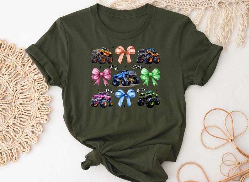 Puede incluir: Camiseta verde oliva con un dise&ntilde;o de monster trucks y lazos. El gr&aacute;fico muestra seis monster trucks de diferentes colores, cada uno con un lazo a juego. Los camiones tienen neum&aacute;ticos grandes y dise&ntilde;os detallados.