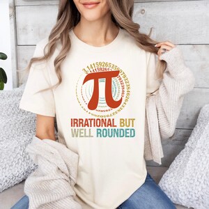 May include: A white t-shirt with a graphic of the mathematical symbol pi surrounded by a circle of numbers. The text "Irrational But Well Rounded" is below the graphic.