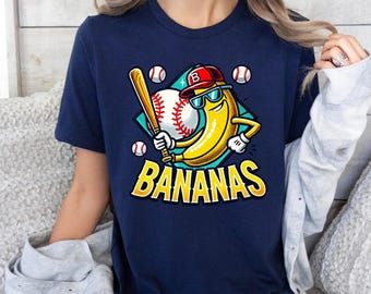 May include: Navy blue t-shirt featuring a cartoon banana wearing sunglasses and a baseball cap, holding a bat. The design includes a baseball and the word "BANANAS" in yellow. The shirt is a casual wear item.