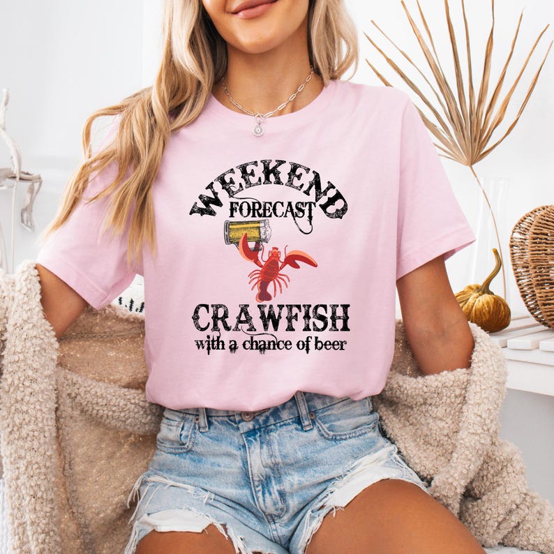May include: Pink t-shirt with a graphic of a crawfish holding a beer and the text "Weekend Forecast Crawfish with a chance of beer".