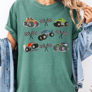 Pode incluir: Camiseta verde com gr&aacute;ficos coloridos de monster trucks e bandeiras quadriculadas. Os caminh&otilde;es s&atilde;o de v&aacute;rias cores, incluindo laranja, verde, azul e roxo. O design &eacute; divertido e adequado para os f&atilde;s de monster trucks.