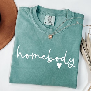 May include: A teal green t-shirt with the text "homebody" in white with a small white heart.